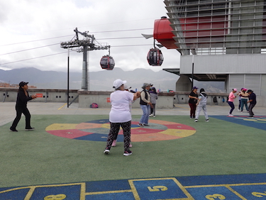 Women exercising on a rooftop with a colorful surface. Cable cars are visible in the background.