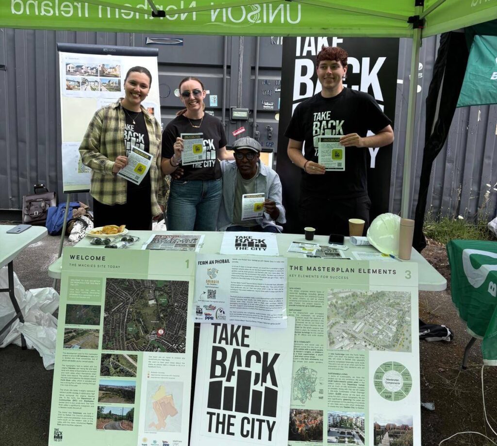 Three campaigners standing at a stand promoting "Take Back the City" initiative